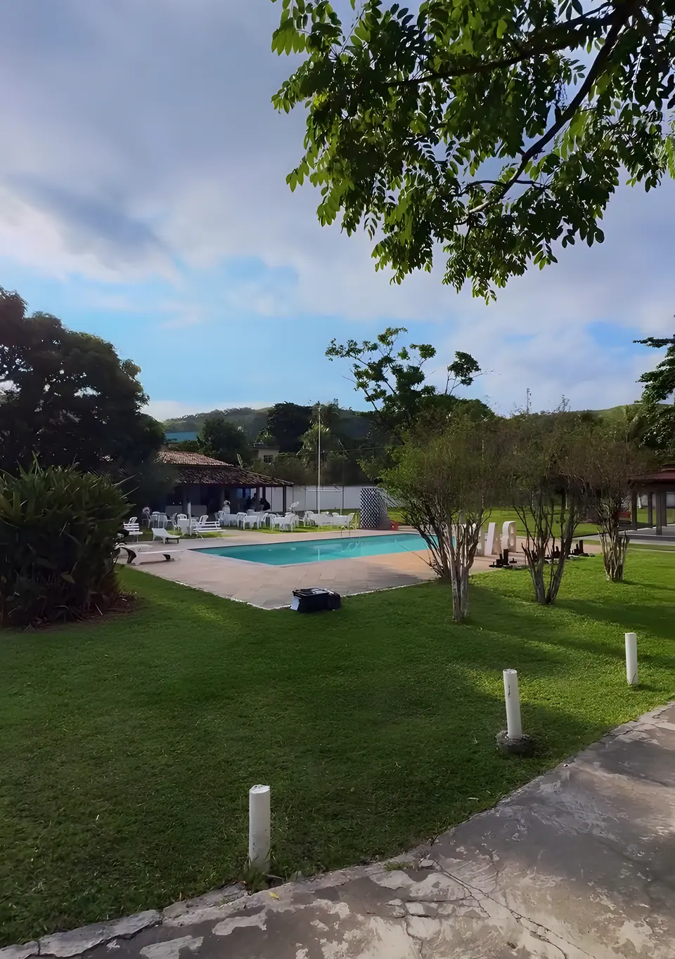 Gramado do Sítio Azul visto da sombra de uma árvore, com a piscina ao fundo