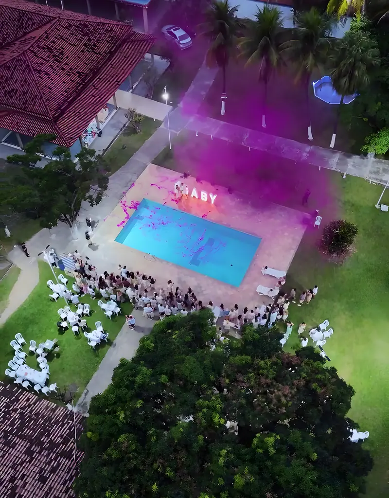 Vista aérea da festa à noite, com a piscina iluminada e fumaça rosa