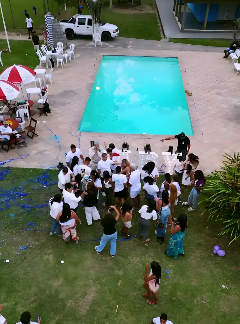 Convidados de branco ao redor da piscina em um chá revelação de dia, visto do alto